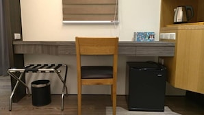 Une cuisine compacte avec une chaise en bois, un réfrigérateur noir, une petite poubelle et une fenêtre avec des stores.
