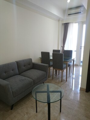 A living room with a grey sofa, a glass coffee table, and a dining area with a table and chairs. - Menteng Park By The Jones (Jakarta)