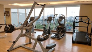 A gym with various exercise equipment, large windows, and a city view. - Menteng Park By The Jones (Jakarta)
