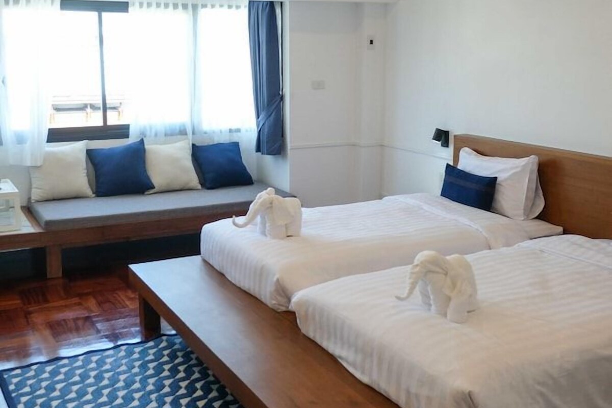 Een hotelkamer met twee bedden, een slaapbank, een houten bankje en een airconditioning.