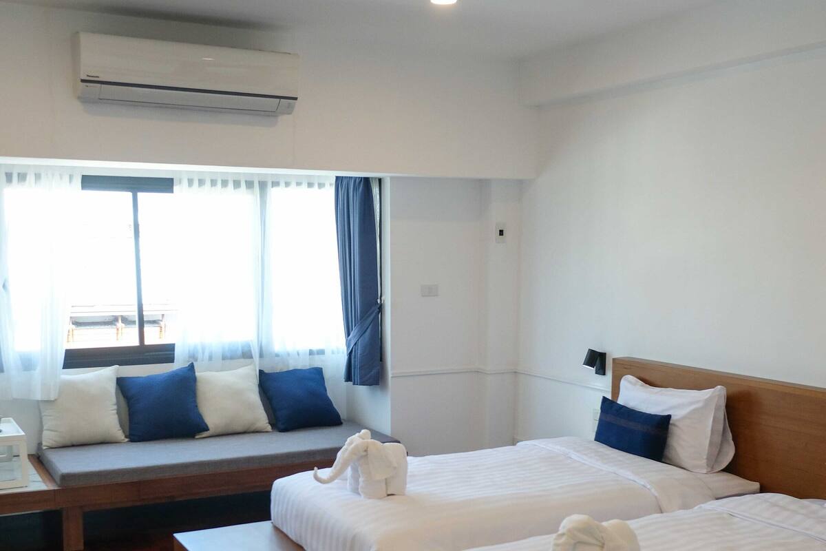 Een hotelkamer met twee bedden, een bankje, een kamerkleed met patroon en een raam met gordijnen.