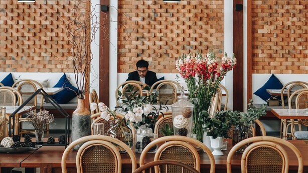 Een restaurant met bakstenen muren, hangende kroonluchters, rieten stoelen en een gedekte tafel met bloemen en kaarsen.