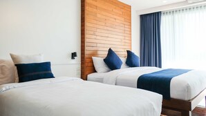Een hotelkamer met twee bedden, een houten hoofdbord, een raam met gordijnen en een airconditioning.