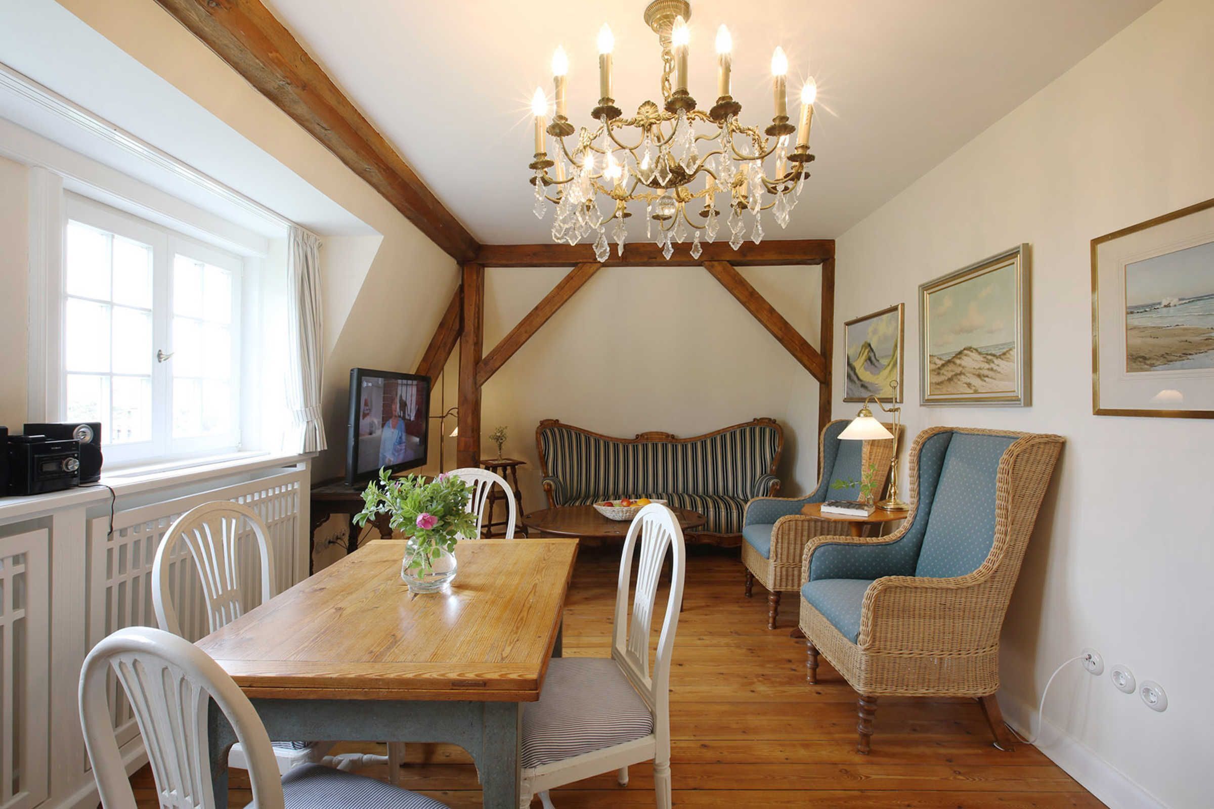 Ein Essbereich mit einem Holztisch, weißen Stühlen, einer Chandelierleuchte, einer Couch und gerahmten Bildern an der Wand.
