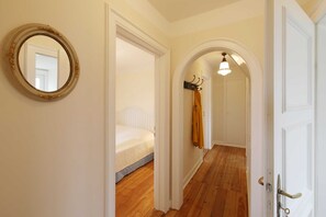 A hallway with wooden flooring, white walls, and a bed in the background.