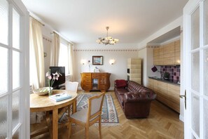 Un comedor con una mesa de madera, sillas y un jarrón de flores. En la sala de estar, hay un sofá de cuero marrón y una alfombra estampada.