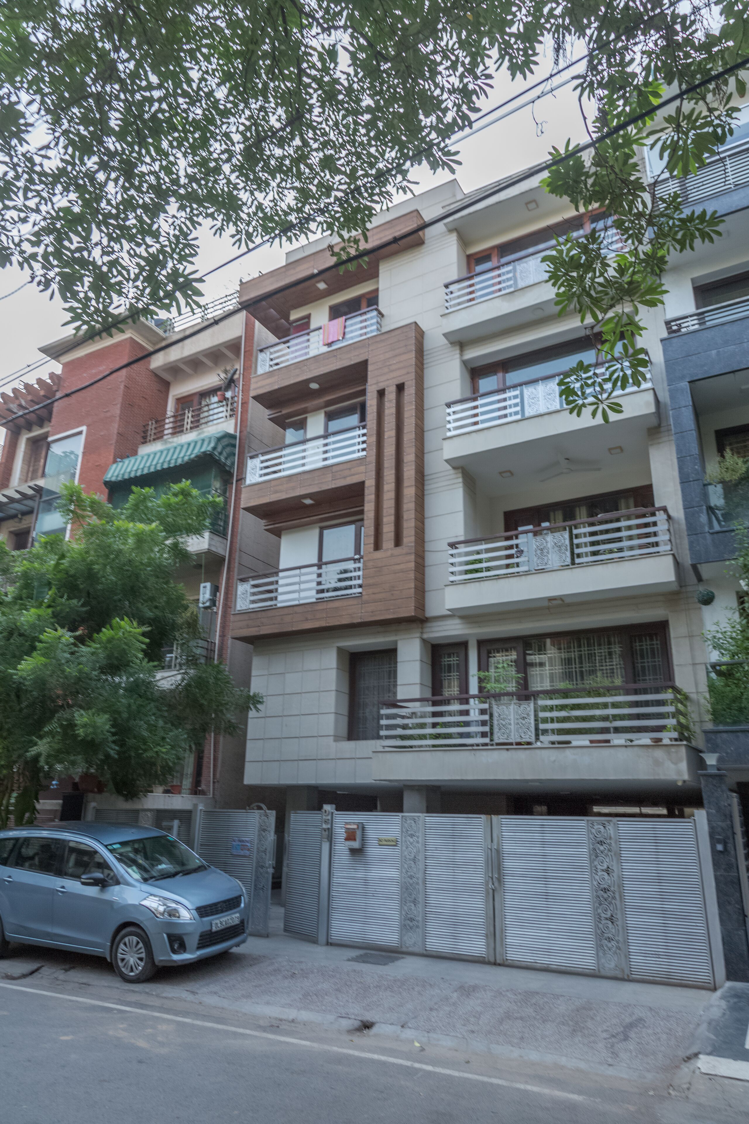 A multi-story residential building with balconies, a gated entrance, and a parked car.
