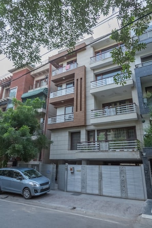 Um edifício residencial com vários andares, varandas, portão fechado e um carro estacionado.