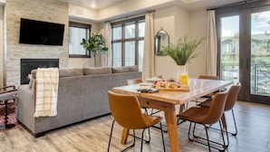 Una sala de estar moderna con chimenea, un sofá, una mesa de comedor con sillas y ventanas grandes que ofrecen vistas.