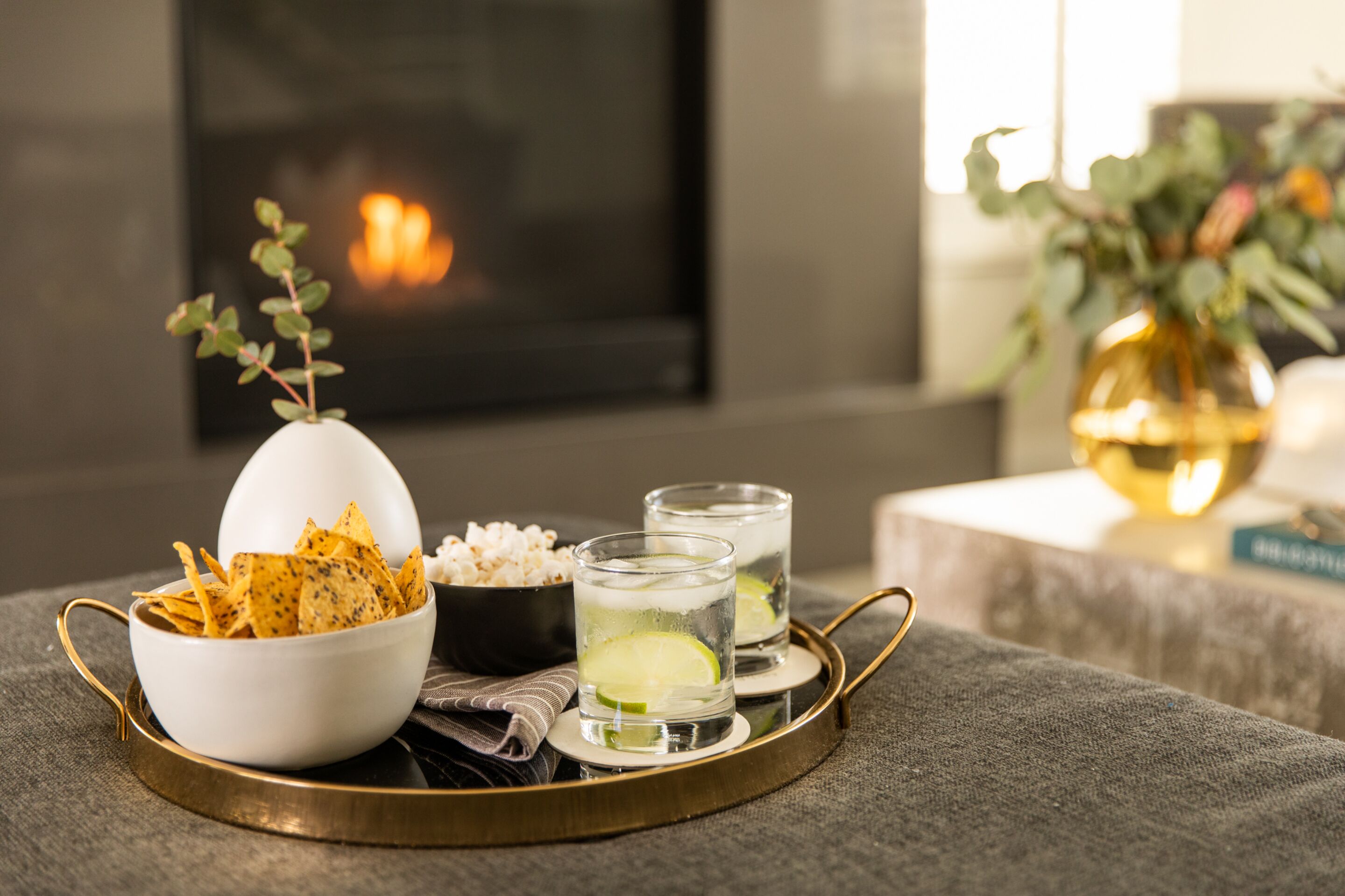 Un plateau avec un bol de chips, un bol de pop-corn et deux verres d’une boisson au goût de citron vert.