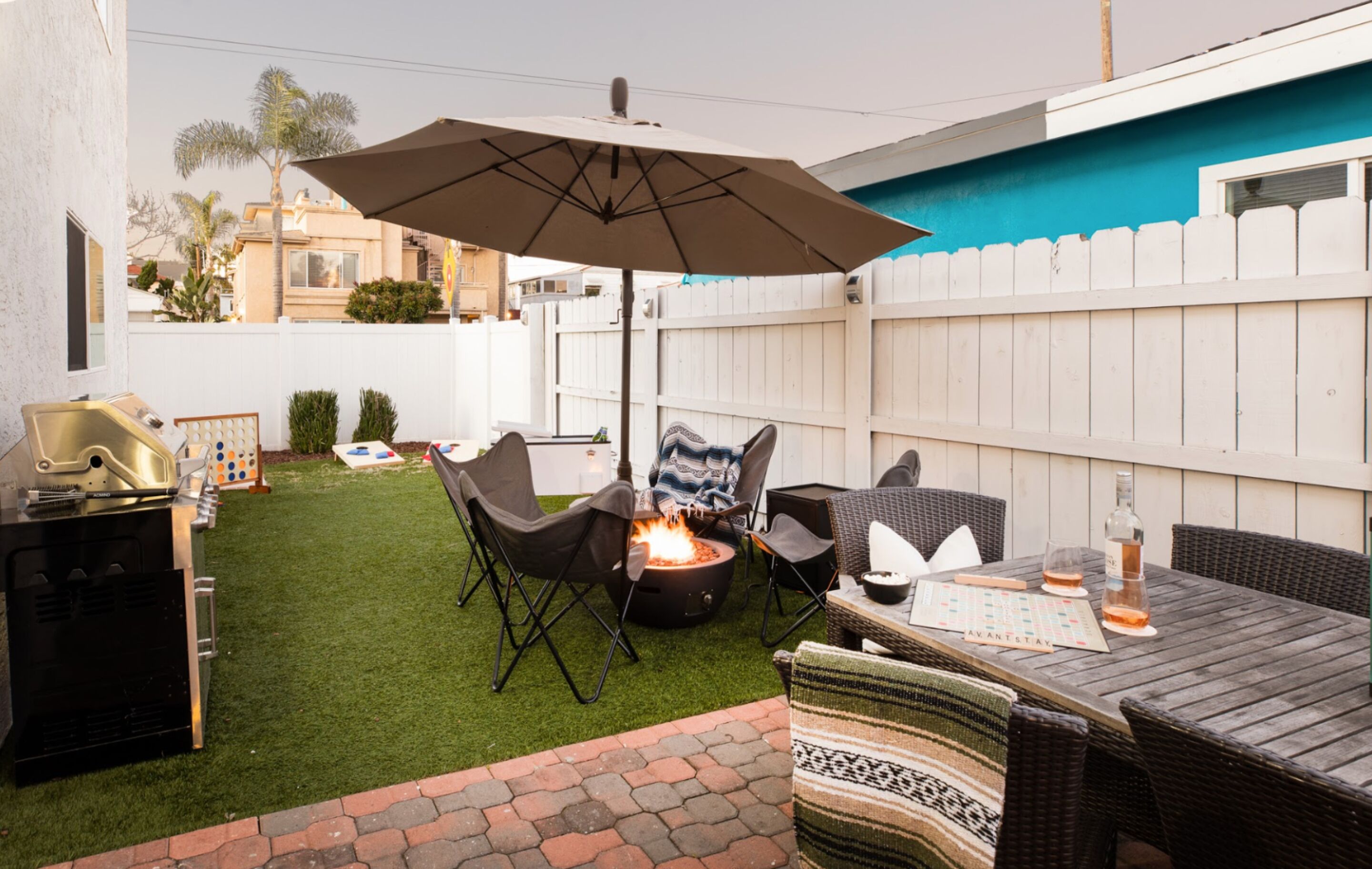 A backyard with a fire pit, outdoor furniture, a grill, and a table with drinks.