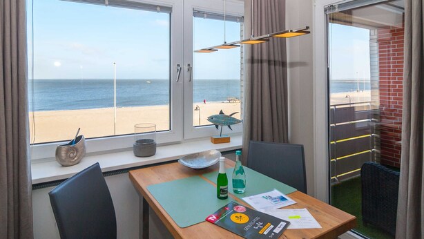 Une pièce avec une table, des chaises, une vue sur la plage et une fenêtre avec des rideaux.
