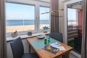 Une pièce avec une table, des chaises, une vue sur la plage et une fenêtre avec des rideaux.