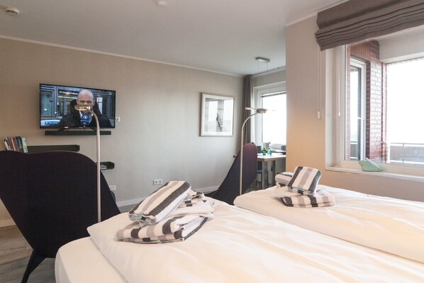 Une chambre d’hôtel avec deux lits, un téléviseur fixé au mur, un bureau avec une chaise et une fenêtre donnant sur un paysage agréable.