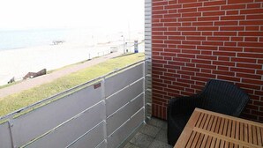 Un balcon donnant sur la plage, un mur en briques et une chaise en osier.