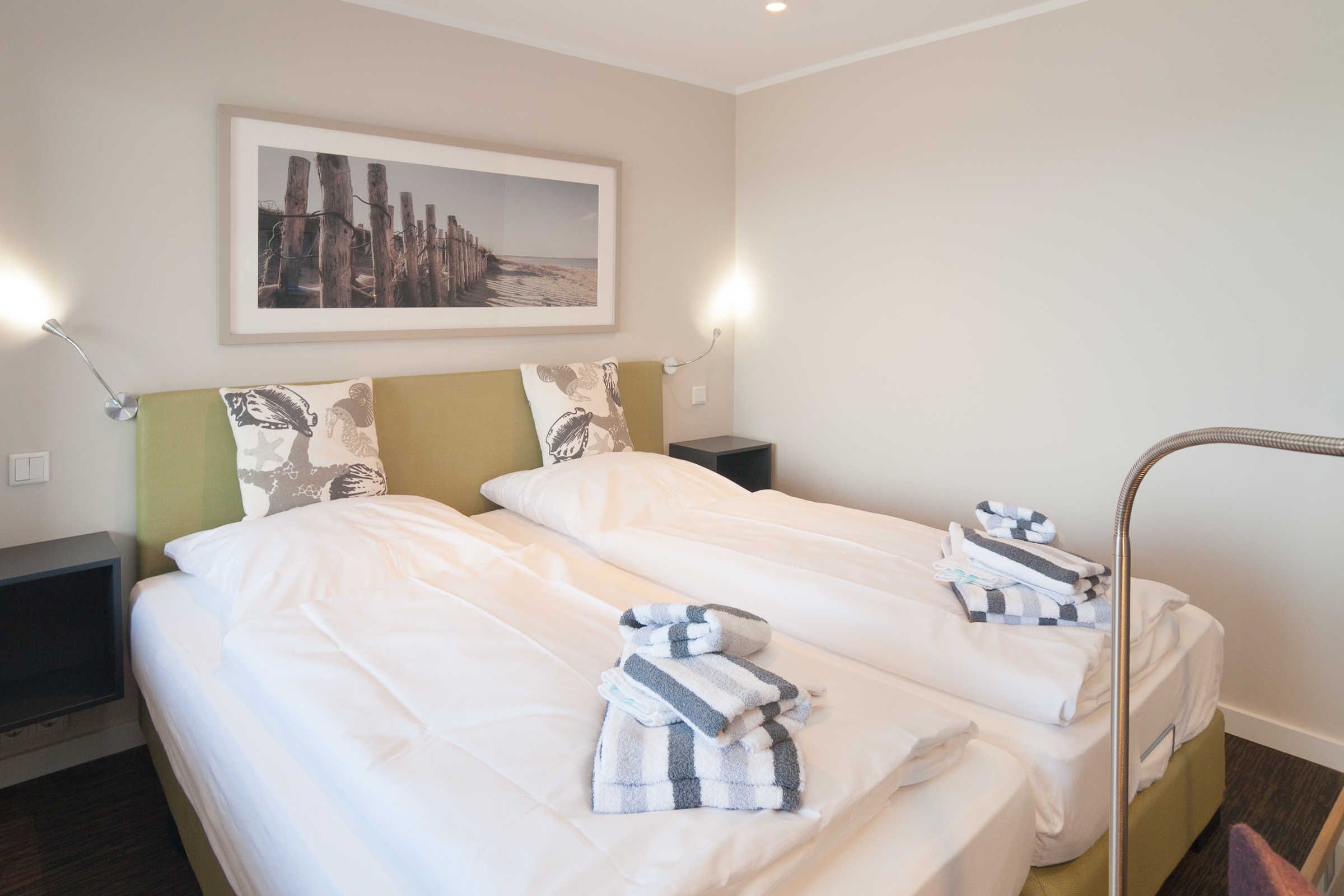 A hotel room with two beds, a framed picture on the wall, and a nightstand with a lamp.
