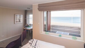 Une chambre d’hôtel avec une grande fenêtre donnant sur la plage, un bureau avec une chaise et un lit avec une serviette à rayures.