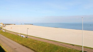 Une plage avec une promenade dallée, des bancs et des lampadaires.