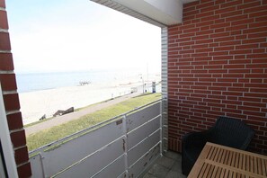 A balcony with a view of the beach, a brick wall, and a wicker chair.