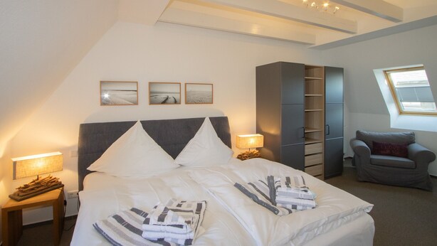 A bedroom with a large bed, bedside tables, a wardrobe, and a window. - House Emilia app. lighthouse (Hörnum (Sylt))