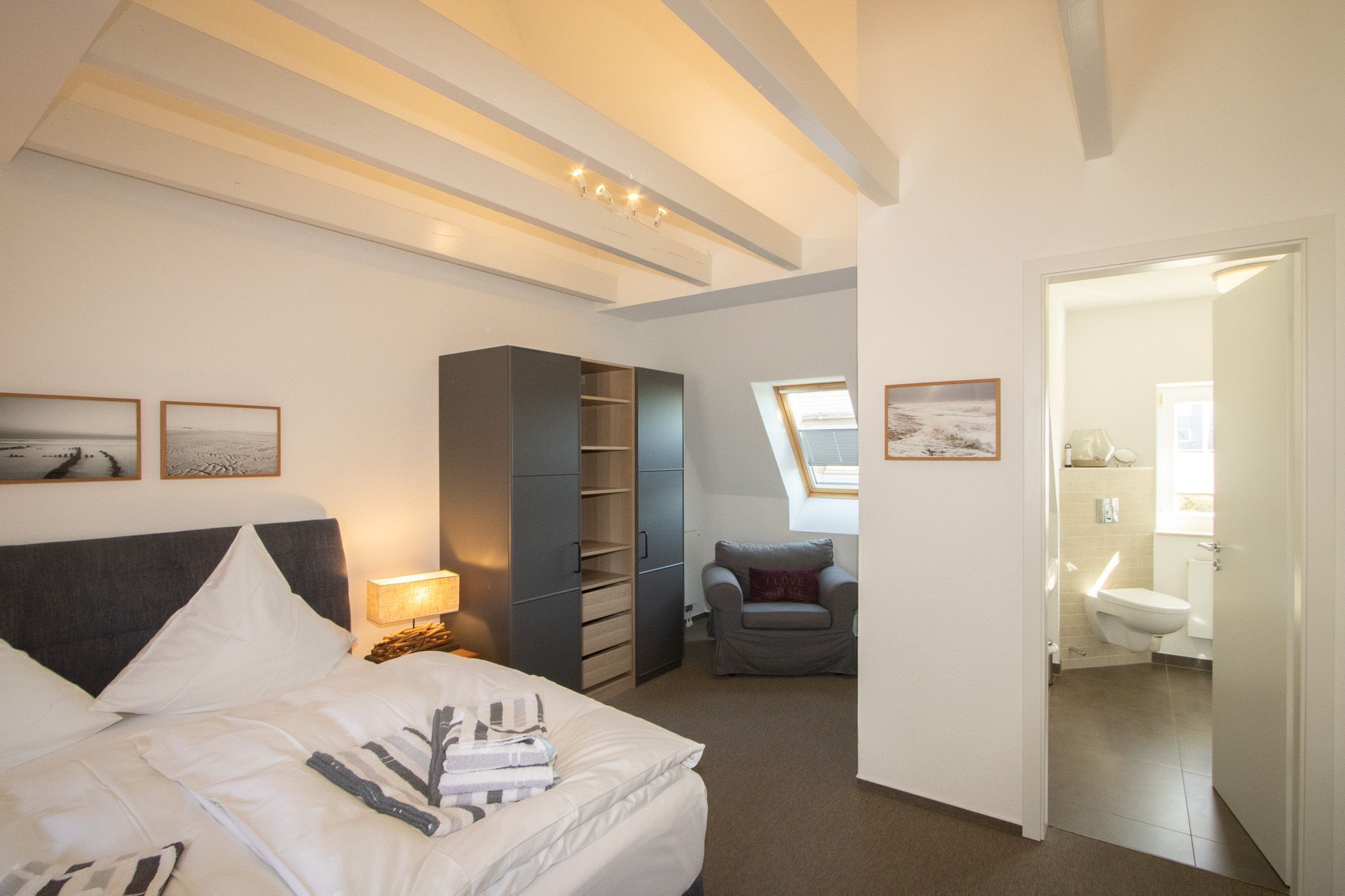 Een slaapkamer met een bed, nachtkastje, lamp, garderobe en uitzicht op de badkamer.