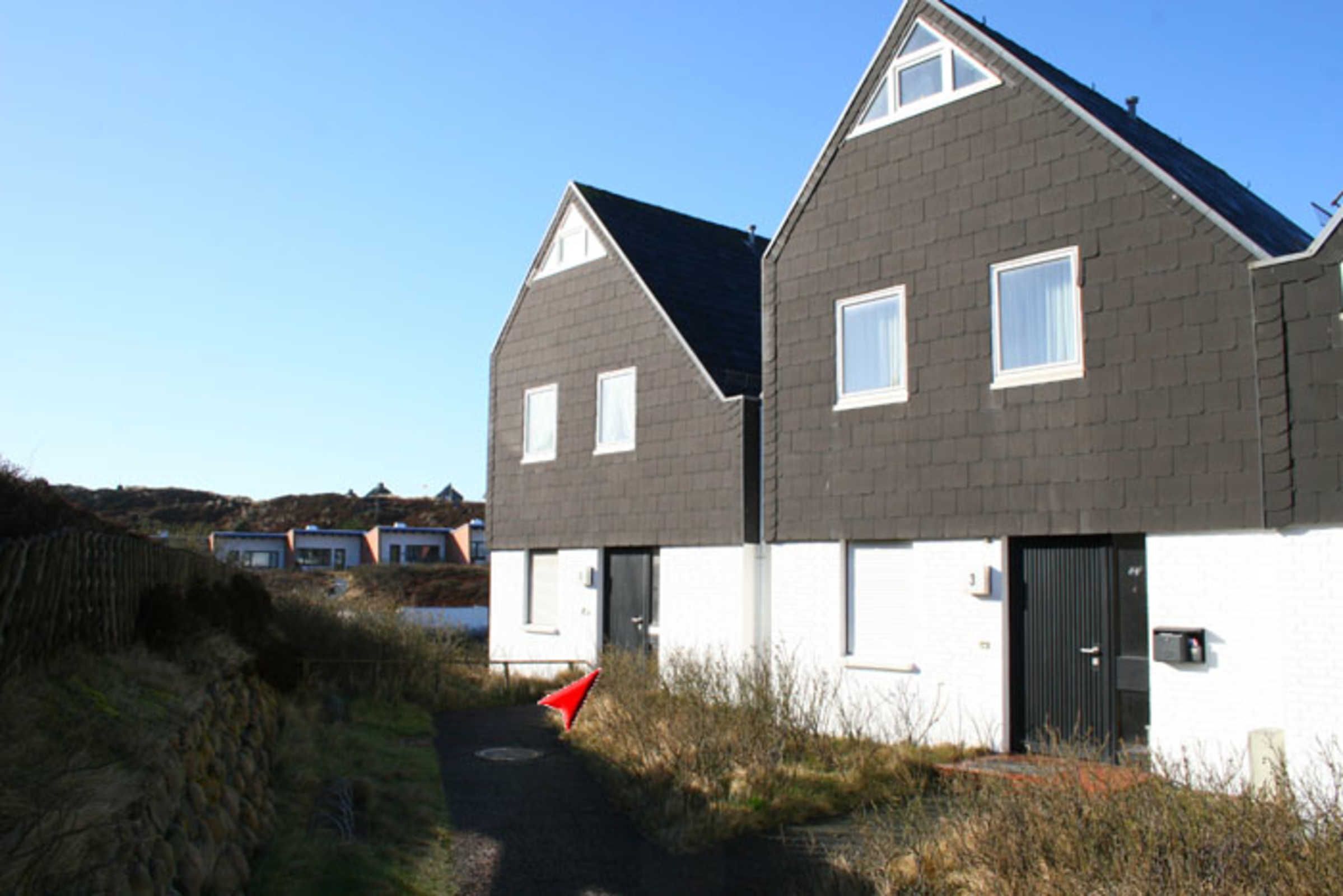 A modern two-story house with a dark grey roof and white walls, featuring a pathway leading to the entrance.