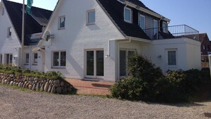 A two-story house with a sloped roof, a balcony on the upper floor, and a gravel driveway. - Holiday beacon (Hörnum (Sylt))
