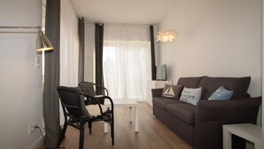 A modern living room with a brown sofa, a white coffee table, a black chair, and a TV on the wall. - Holiday beacon (Hörnum (Sylt))
