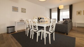 A modern living room with a dining area, a grey sofa, and a white table with chairs. - Holiday beacon (Hörnum (Sylt))