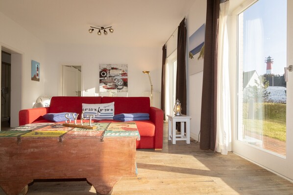 A modern living room with a red sofa, a wooden coffee table with a map, and a view of a lighthouse through large windows.