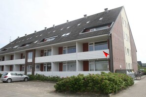 A multi-story residential building with a sloped roof, balconies, and a parking area.