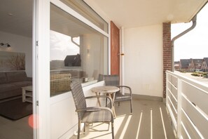 A balcony with wicker furniture, a small table, and a view of the neighborhood. - Holiday Ferlings (Hörnum (Sylt))