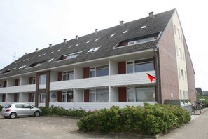 A multi-story residential building with a sloped roof, balconies, and a parking area.