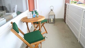 Pieni parveke, jossa on pyöreä puupöytä ja kaksi vihreää, pehmustettua tuolia. Pöydällä on pulloja ja lyhty.