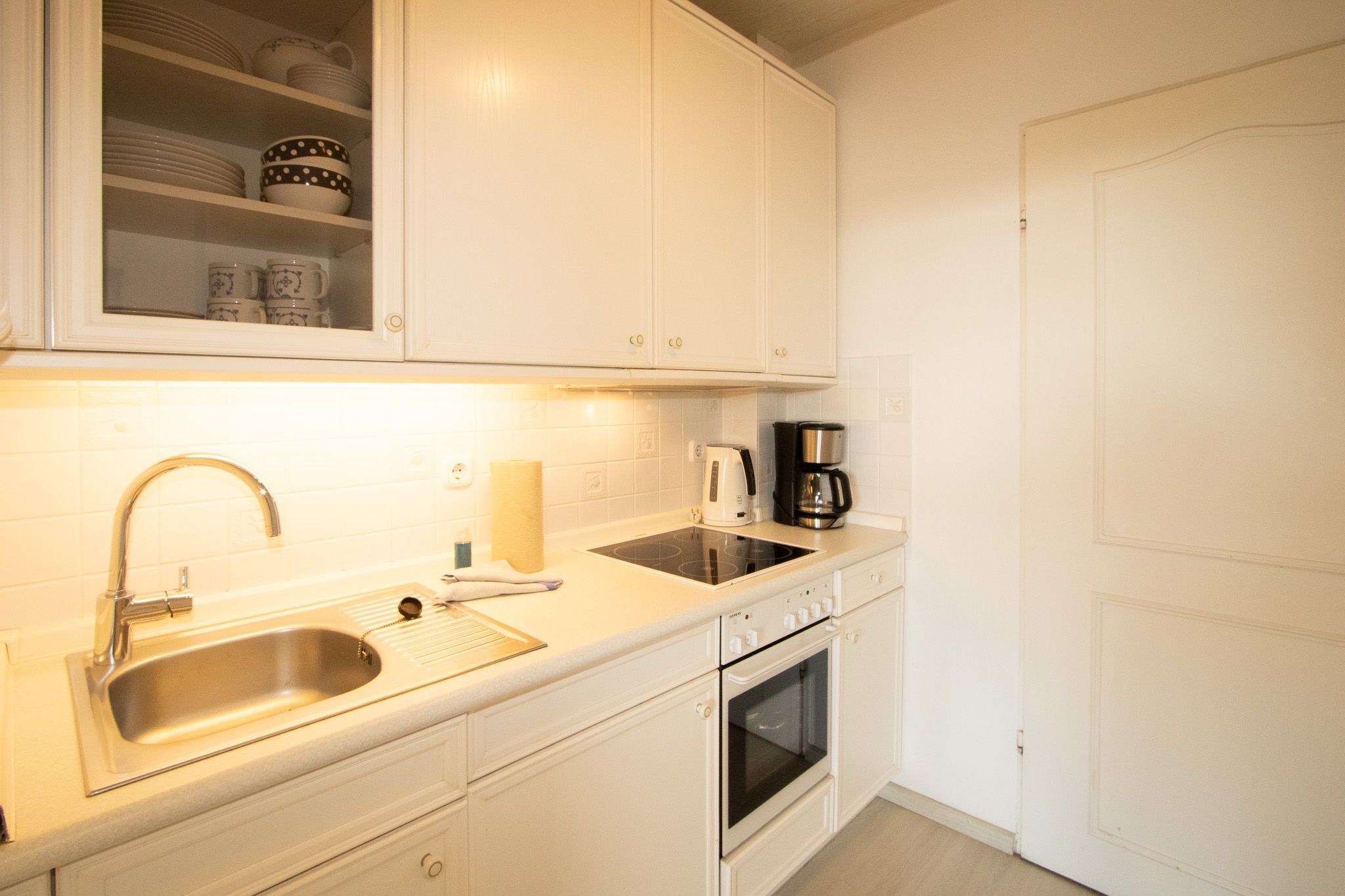 Een keuken met witte kasten, een roestvrijstalen spoelbak, een koffiezetapparaat en een oven.