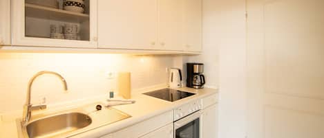 Een keuken met witte kasten, een roestvrijstalen spoelbak, een koffiezetapparaat en een oven.