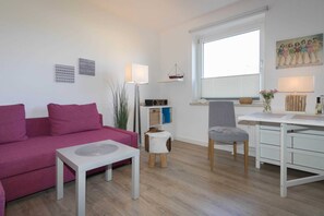 Ein modernes Wohnzimmer mit einem rosafarbenen Sofa, einem weißen Tisch, einem grauen Sessel und einem weißen Schreibtisch.