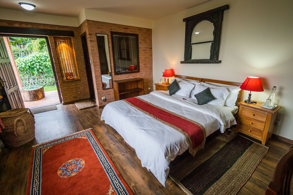 Un dormitorio con una cama grande, mesitas de noche de madera, colcha a rayas rojas y blancas y vista al exterior desde una puerta abierta.