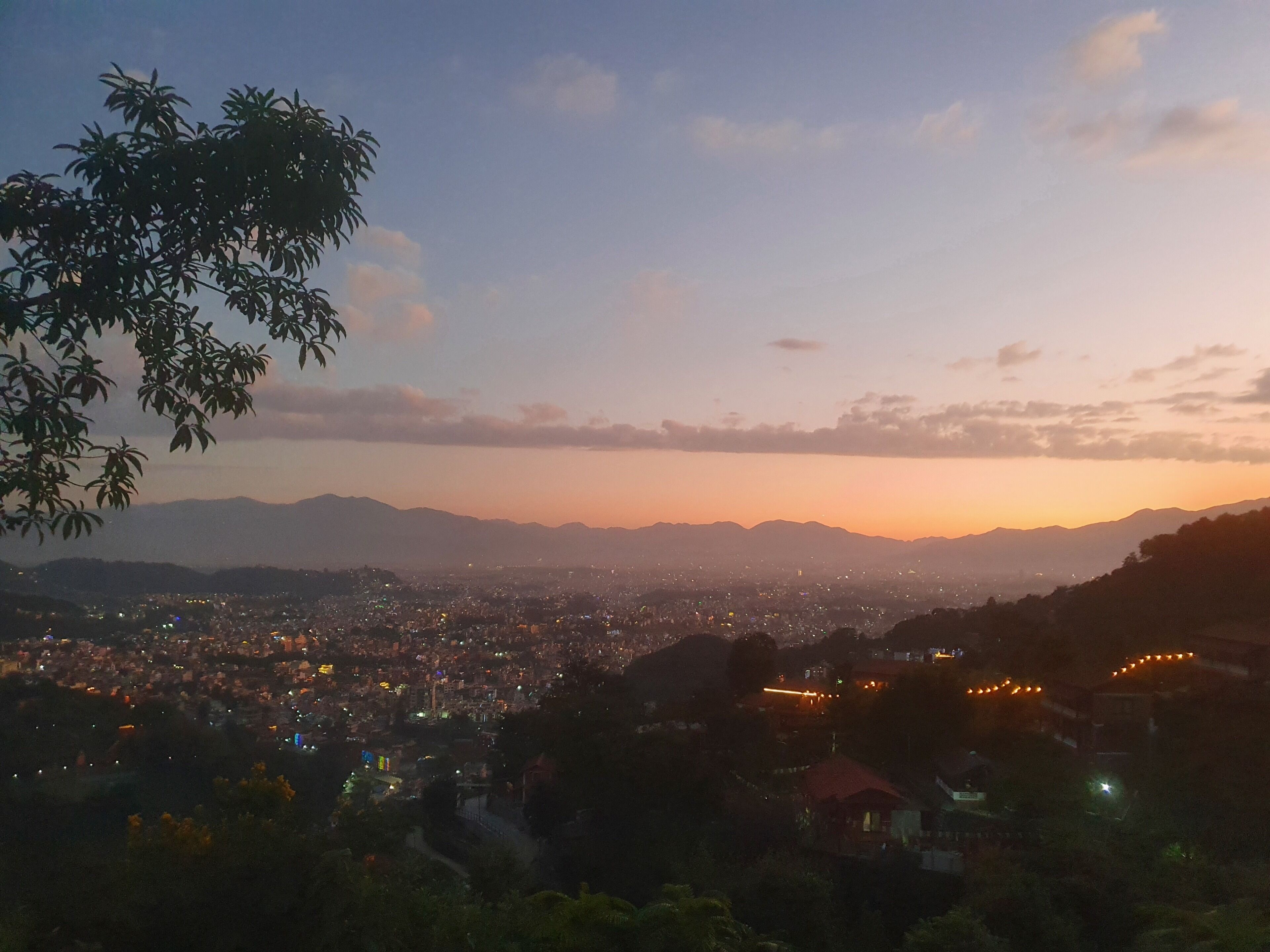 Una vista panoramica di una città al crepuscolo con una catena montuosa sullo sfondo.