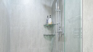 Un espace douche moderne doté d’une porte en verre, d’un pommeau de douche à main et d’un robinet mural.