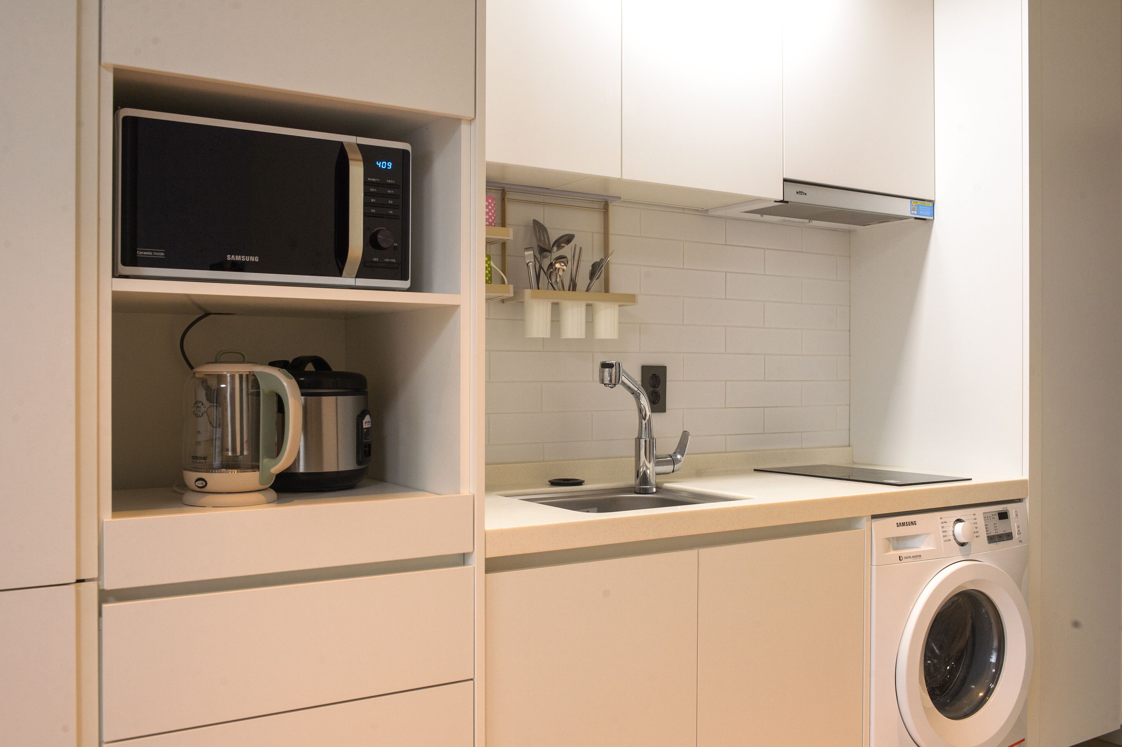Cocina compacta equipada con microondas, hervidor, lavabo y lavadora.
