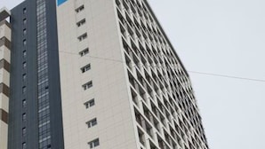 Un hôtel à plusieurs étages, doté d’une façade moderne, qui se distingue par une grande banderole bleue et une série de fenêtres sur la façade.