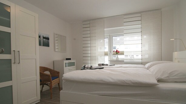 Ein Schlafzimmer mit Bett, Stuhl, Schreibtisch und einem Fenster mit Jalousien.
