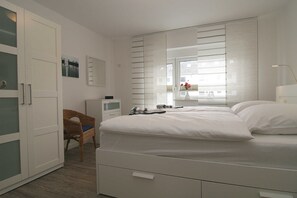 A bedroom with a bed, a chair, a desk, and a window with blinds.