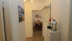 Ein Flur, der in einen Essbereich mit einem Holztisch und Stühlen führt. An der Wand hängt ein Gemälde, und über einem weißen Schrank steht eine Laterne.