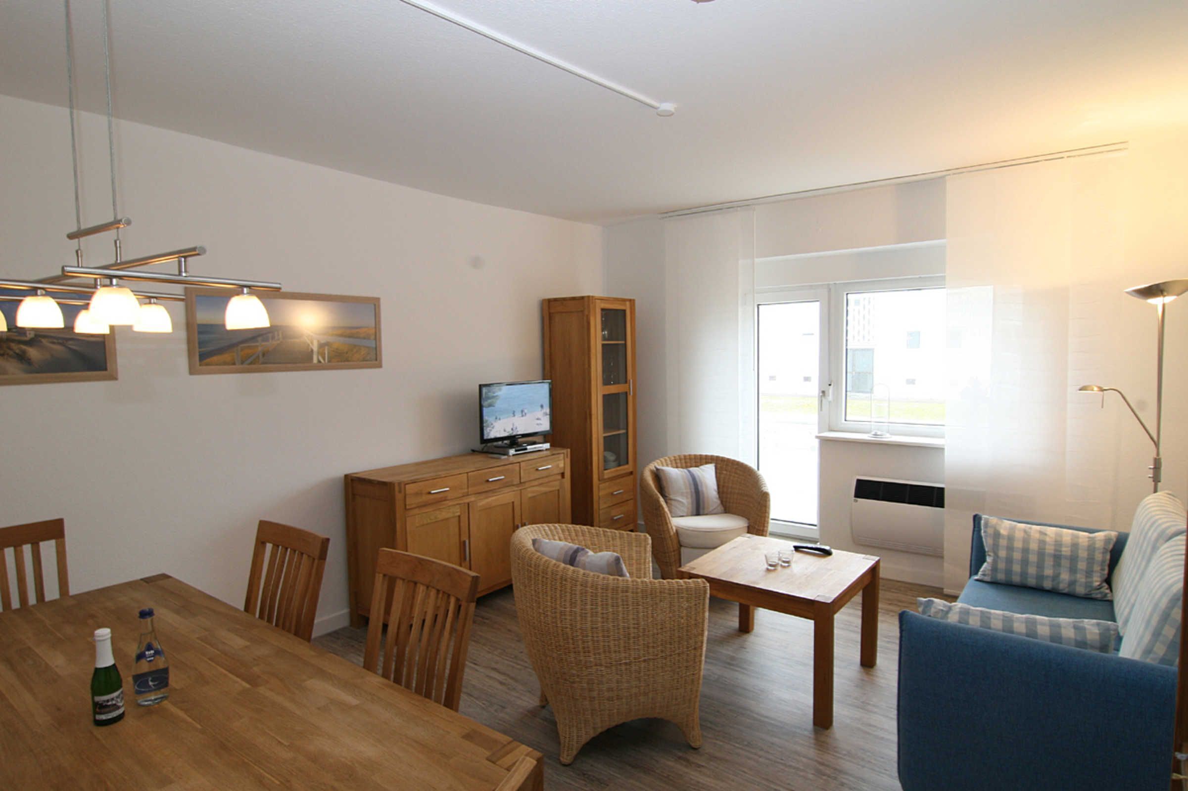 A living room with a wooden dining table, wicker chairs, a sofa, and a television on a cabinet.