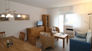 Ein Wohnzimmer mit einem Holzesstisch, Korbstühlen, einer Couch und einem Fernseher auf einem Schrank.