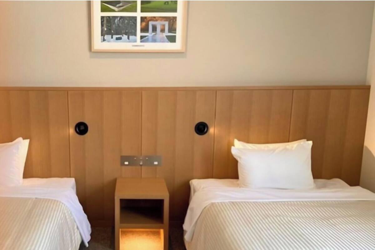 Habitación de hotel con dos camas, cabecera de madera, una mesita de noche pequeña y un cuadro enmarcado en la pared.