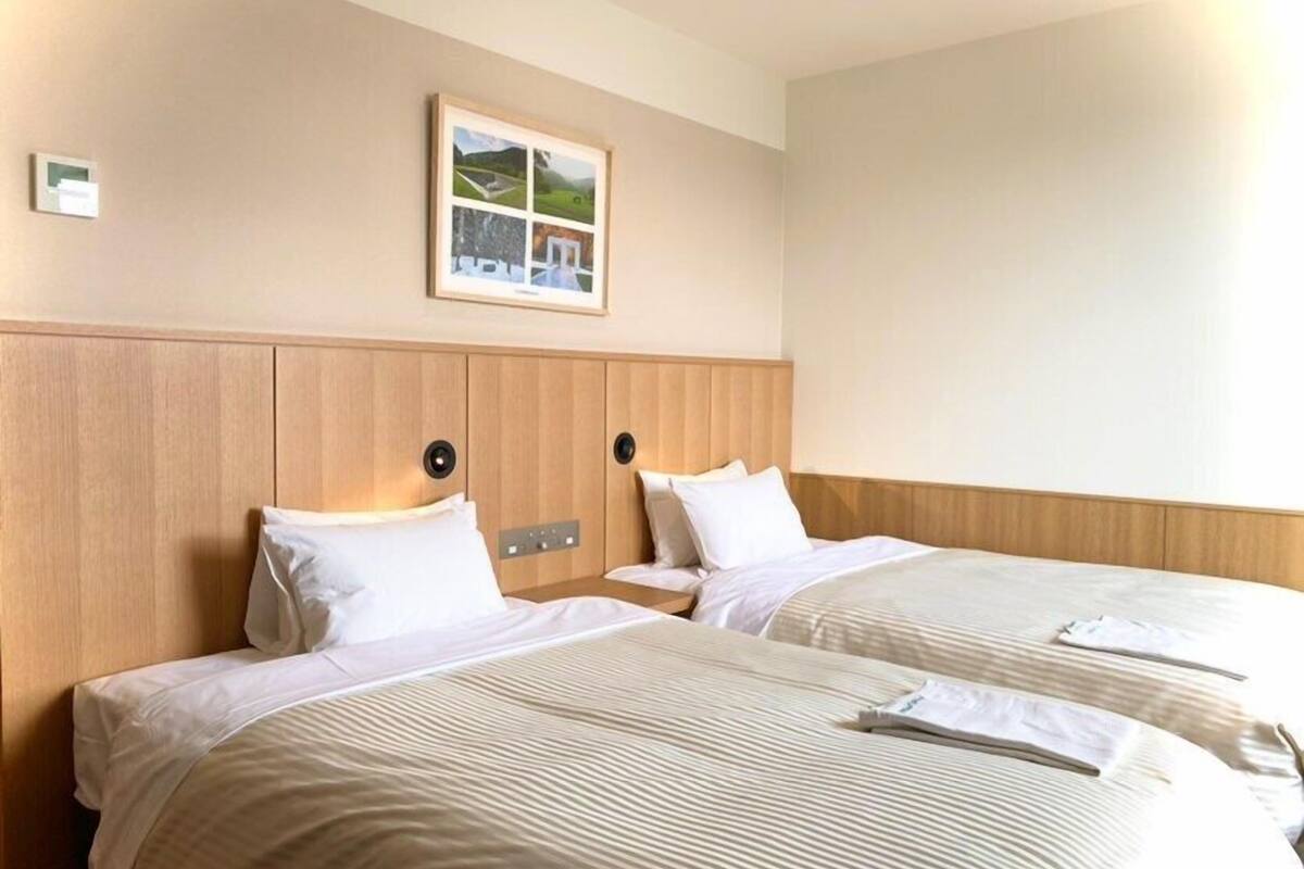 A hotel room with two beds, a wooden headboard, a framed picture on the wall, and a bedside table with a lamp.