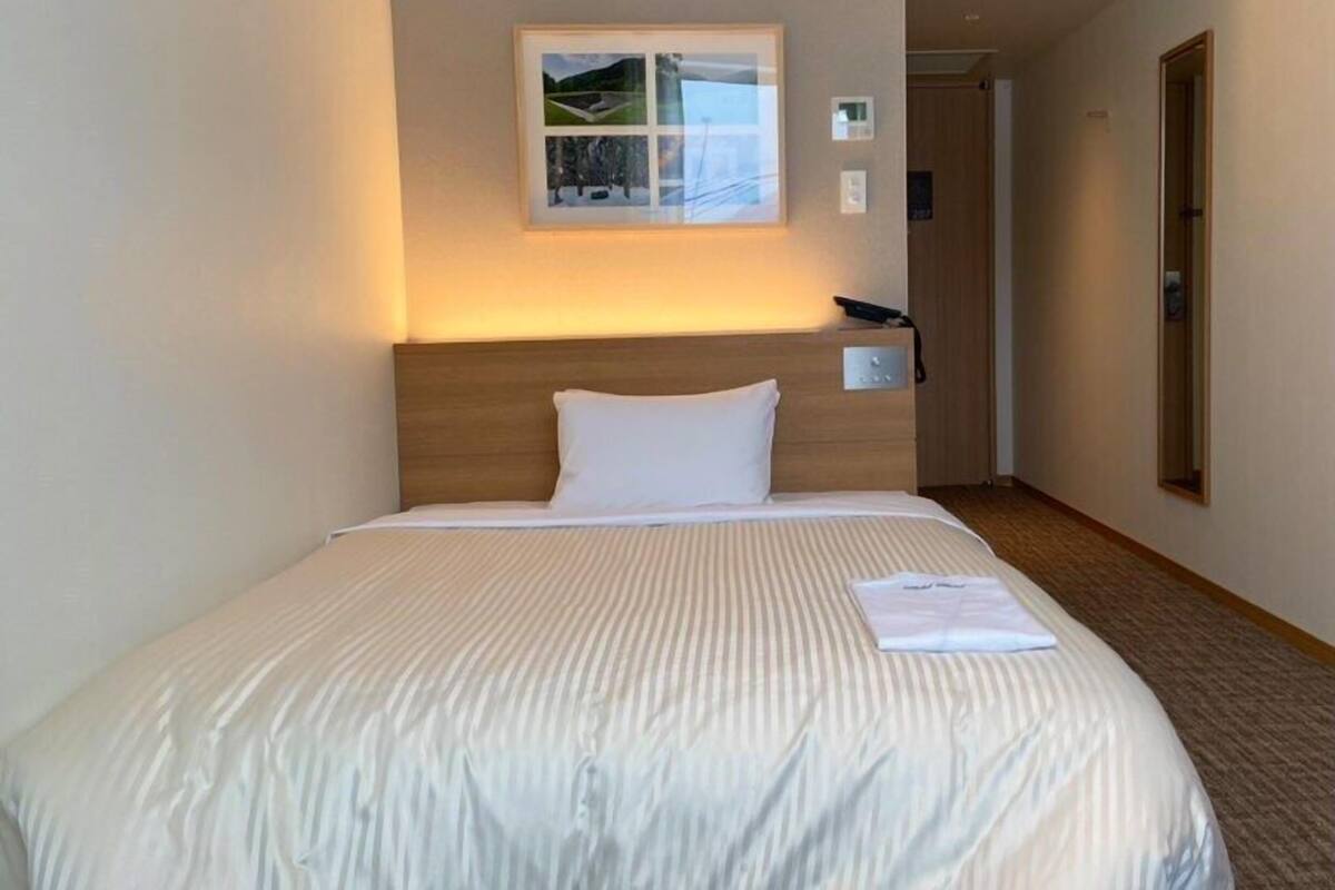 A hotel room with a neatly made bed, a framed picture on the wall, and a bedside telephone.